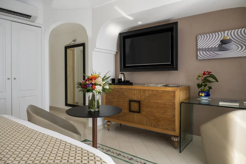 Camera d'albergo moderna con TV a schermo piatto, fiori freschi e arredamento elegante.