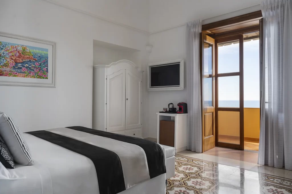 Camera luminosa con balcone vista mare, letto matrimoniale e arredamento elegante.