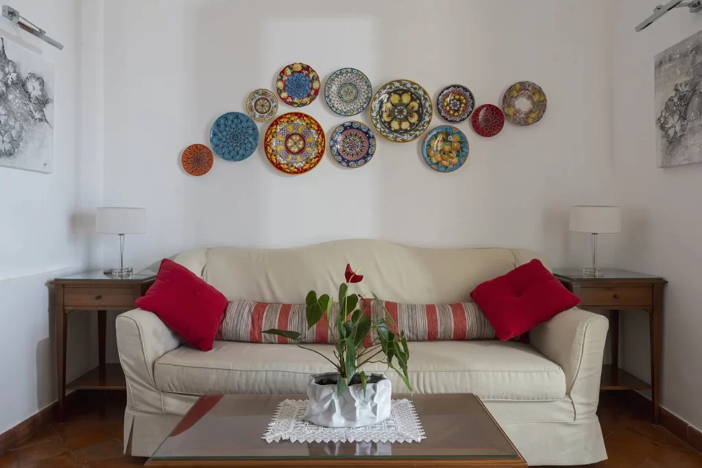 Soggiorno accogliente con divano bianco, cuscini rossi e piatti decorativi appesi al muro.
