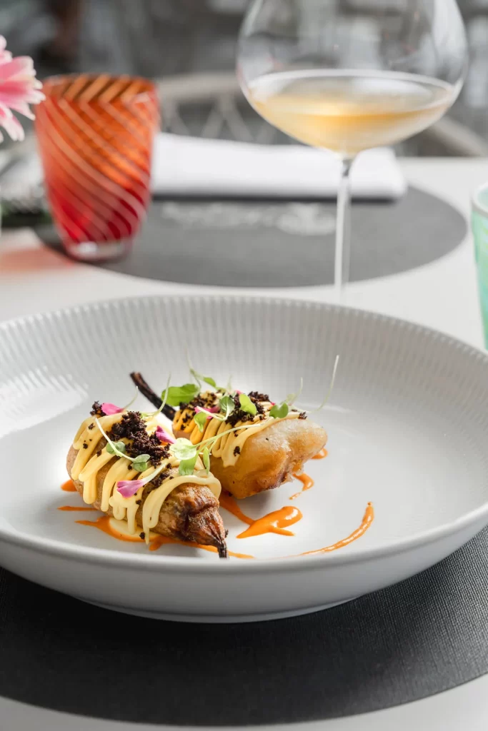 Piatto gourmet con presentazione raffinata e bicchiere di vino bianco.