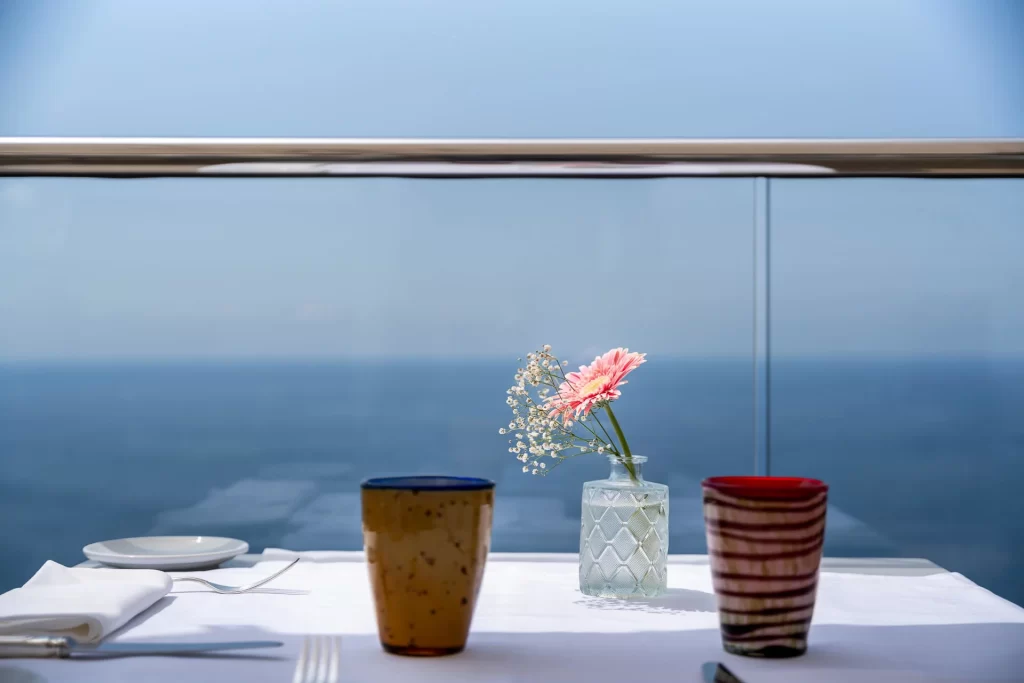 Un tavolo apparecchiato con due tazze e un vaso con fiori, affacciato su una vista marina.