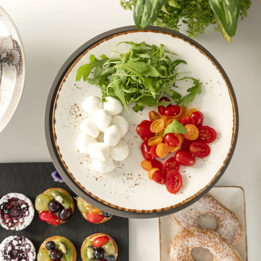 Un piatto con rucola, pomodorini e mozzarelline, circondato da dolci e pane.