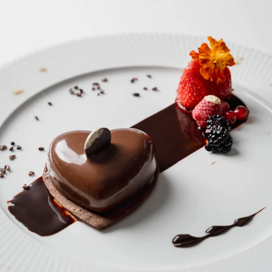 Dolce al cioccolato a forma di cuore decorato con frutti di bosco e una salsa al cioccolato.